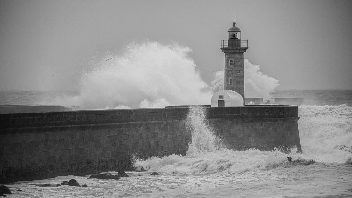 A lighthouse standing firm against crashing waves in black and white